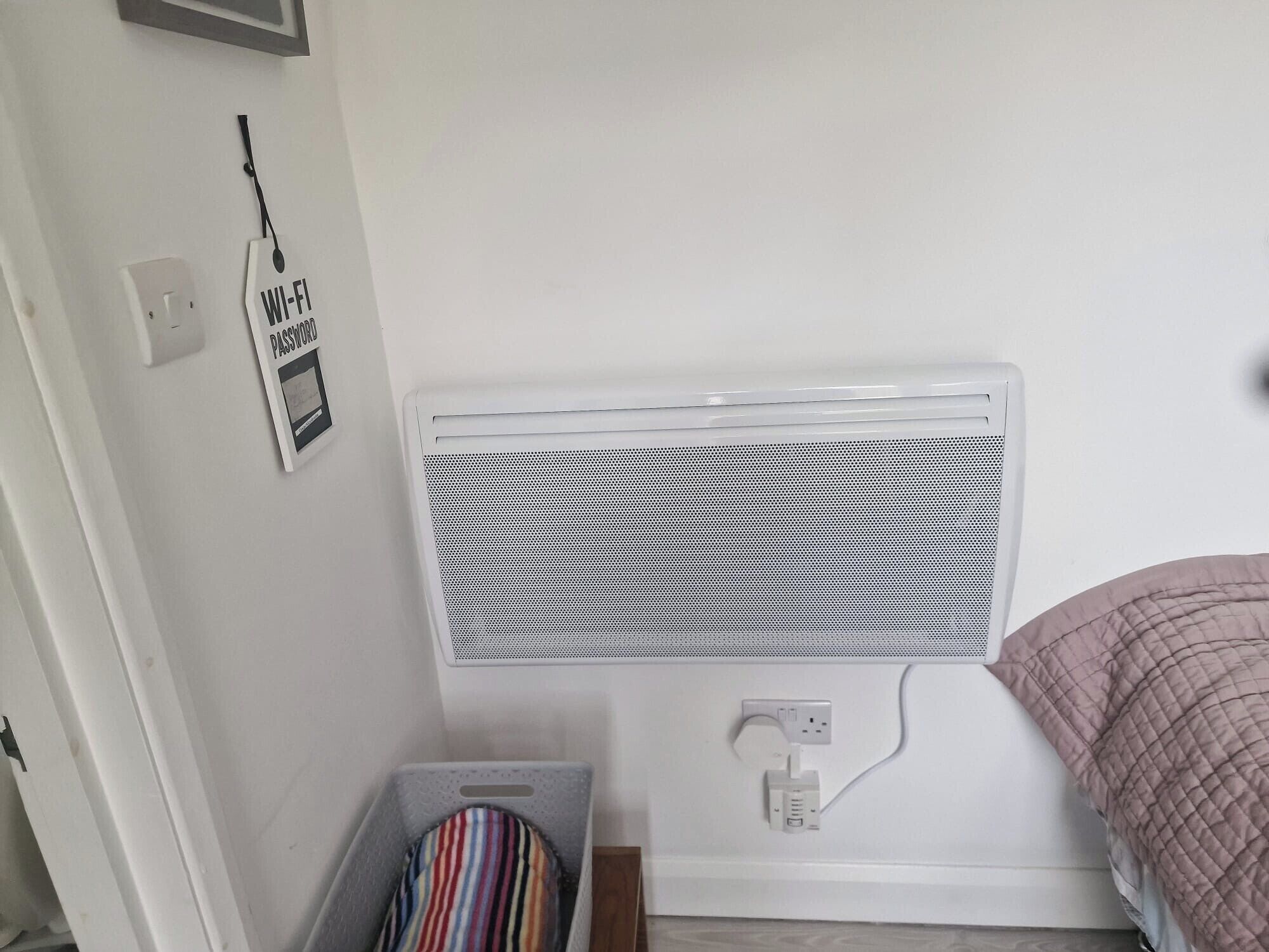 A bedroom with a white radiator, a striped pillow in a gray laundry basket, and a wall-mounted power outlet.