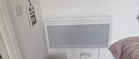 A bedroom with a white radiator, a striped pillow in a gray laundry basket, and a wall-mounted power outlet.