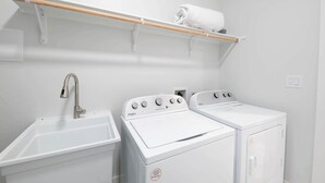 A laundry room with a sink, two white Whirlpool washers, and a wooden shelf with a rolled towel. - Coral Cove (South Padre Island)
