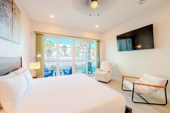 A hotel room with a large bed, a TV mounted on the wall, and a balcony with outdoor furniture.