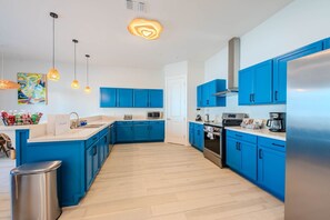 A modern kitchen with blue cabinets, stainless steel appliances, and a wooden floor. - Coral Cove (South Padre Island)