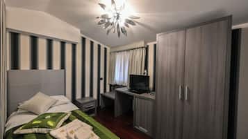 A hotel room with a bed, a desk with a computer, a television, and a wardrobe.