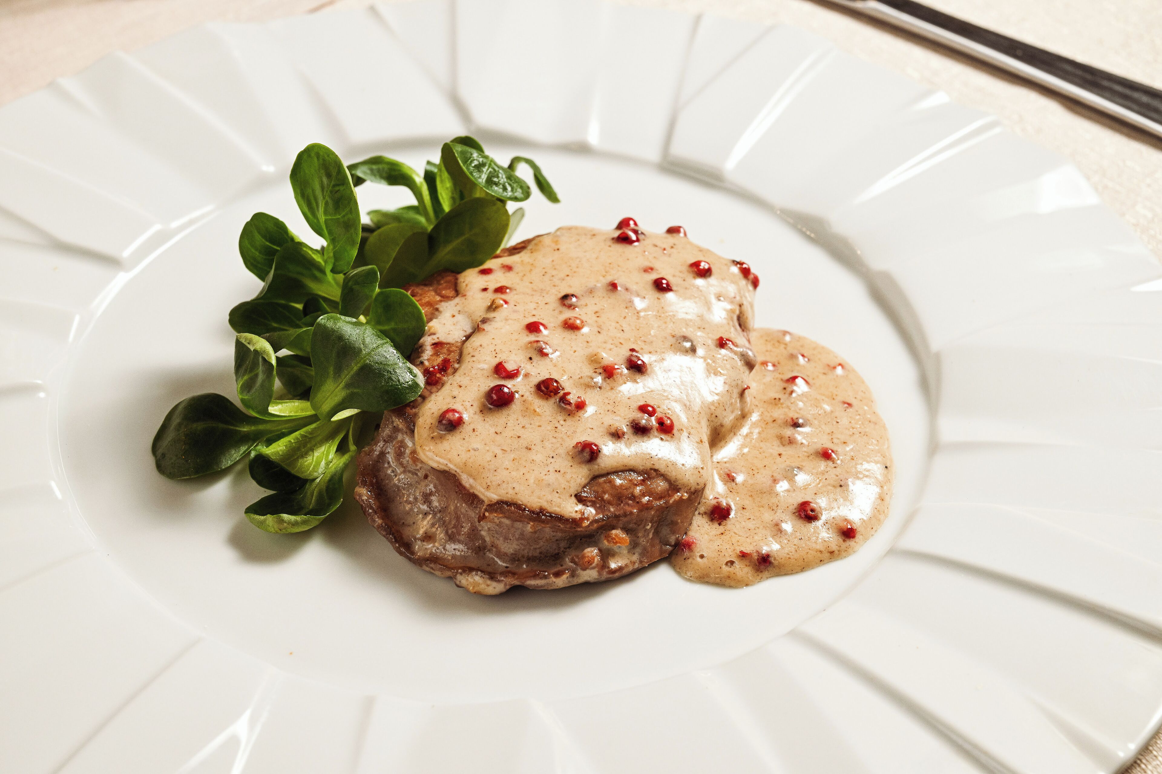 A plate with a meat dish, sauce, and greens.