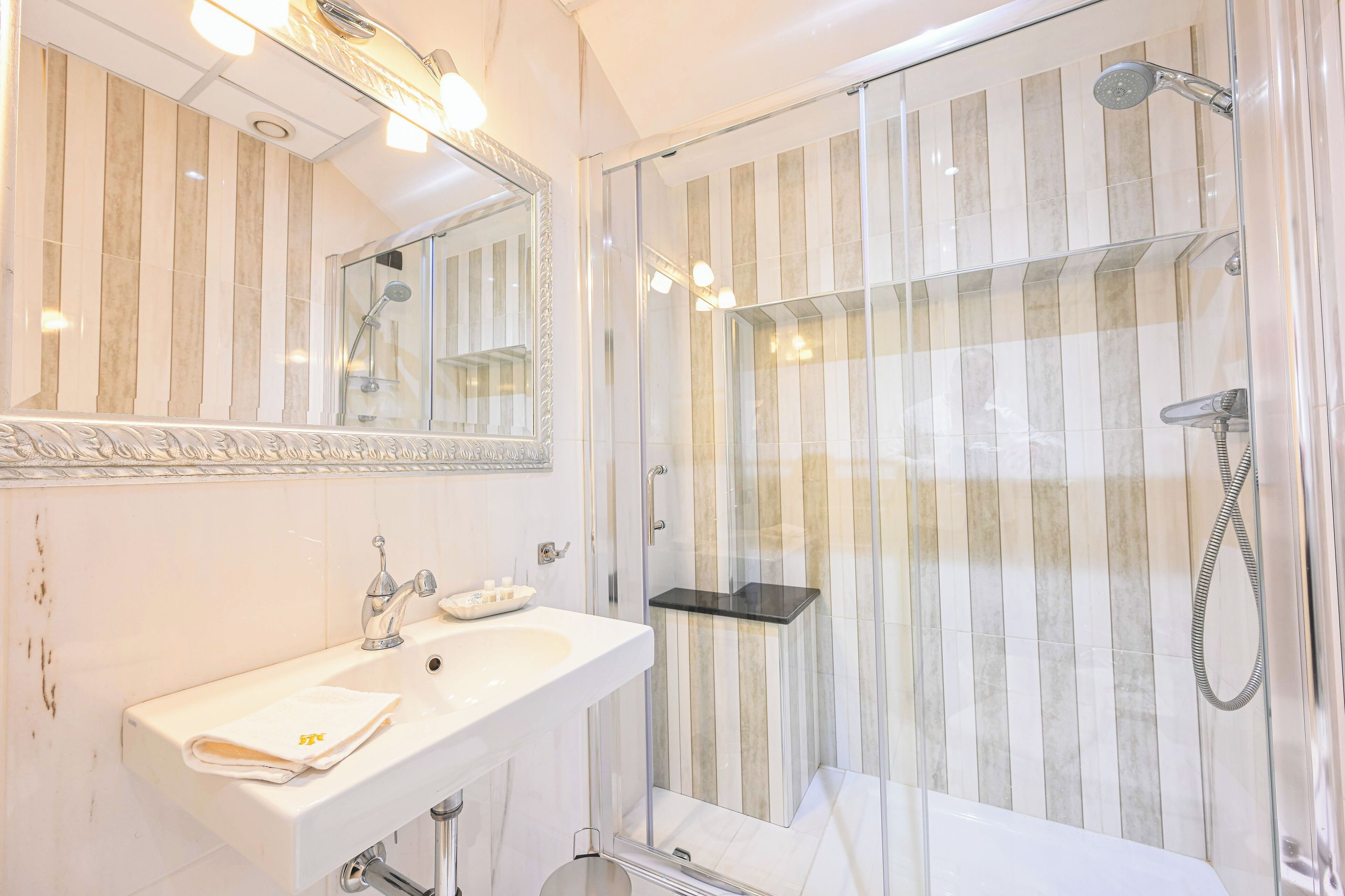 Une salle de bain moderne avec une douche à l’italienne en verre, un lavabo blanc avec un miroir et une serviette posée sur le comptoir.