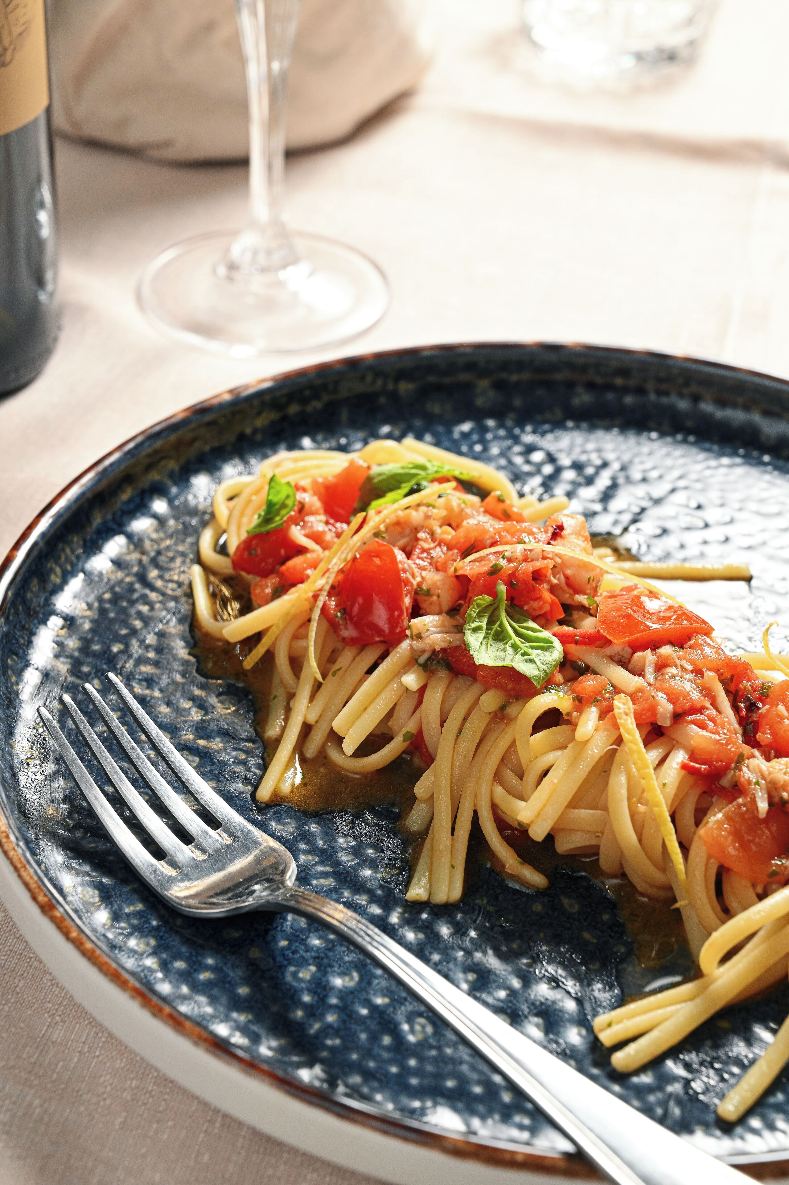 A plate of spaghetti with tomato sauce and basil, a fork, and a glass of wine on a table.