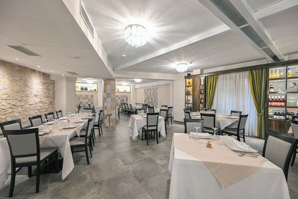 A restaurant with multiple tables set for dining, a stone wall, and a bar area with bottles. - Hotel Mastrodattia (Celano)