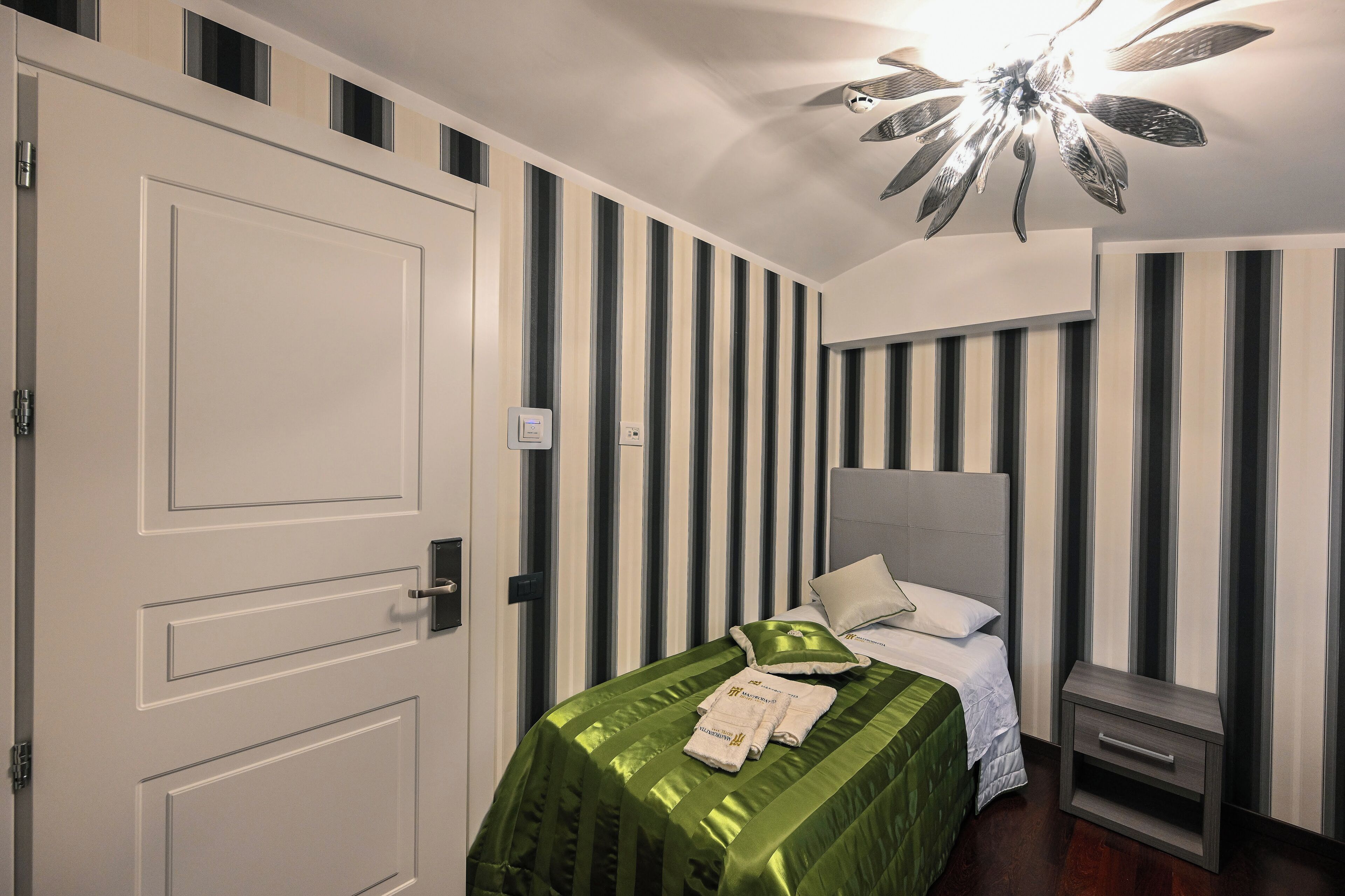 Ein Schlafzimmer mit einer gestreiften Wand, einem Bett mit grüner Bettdecke, einem Nachttisch und einem Deckenventilator.