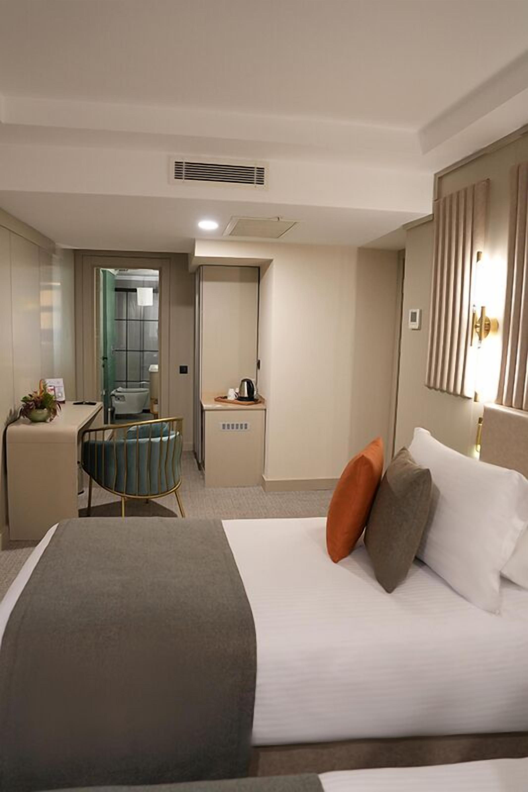 A hotel room with a bed, a desk, a chair, a mirror, and a door leading to a bathroom.