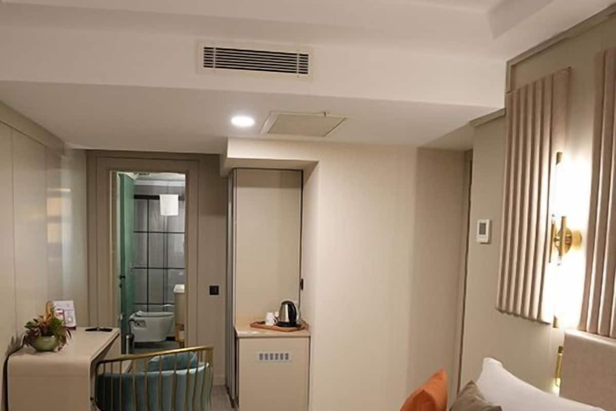 A hotel room with a bed, a desk, a chair, a mirror, and a door leading to a bathroom.