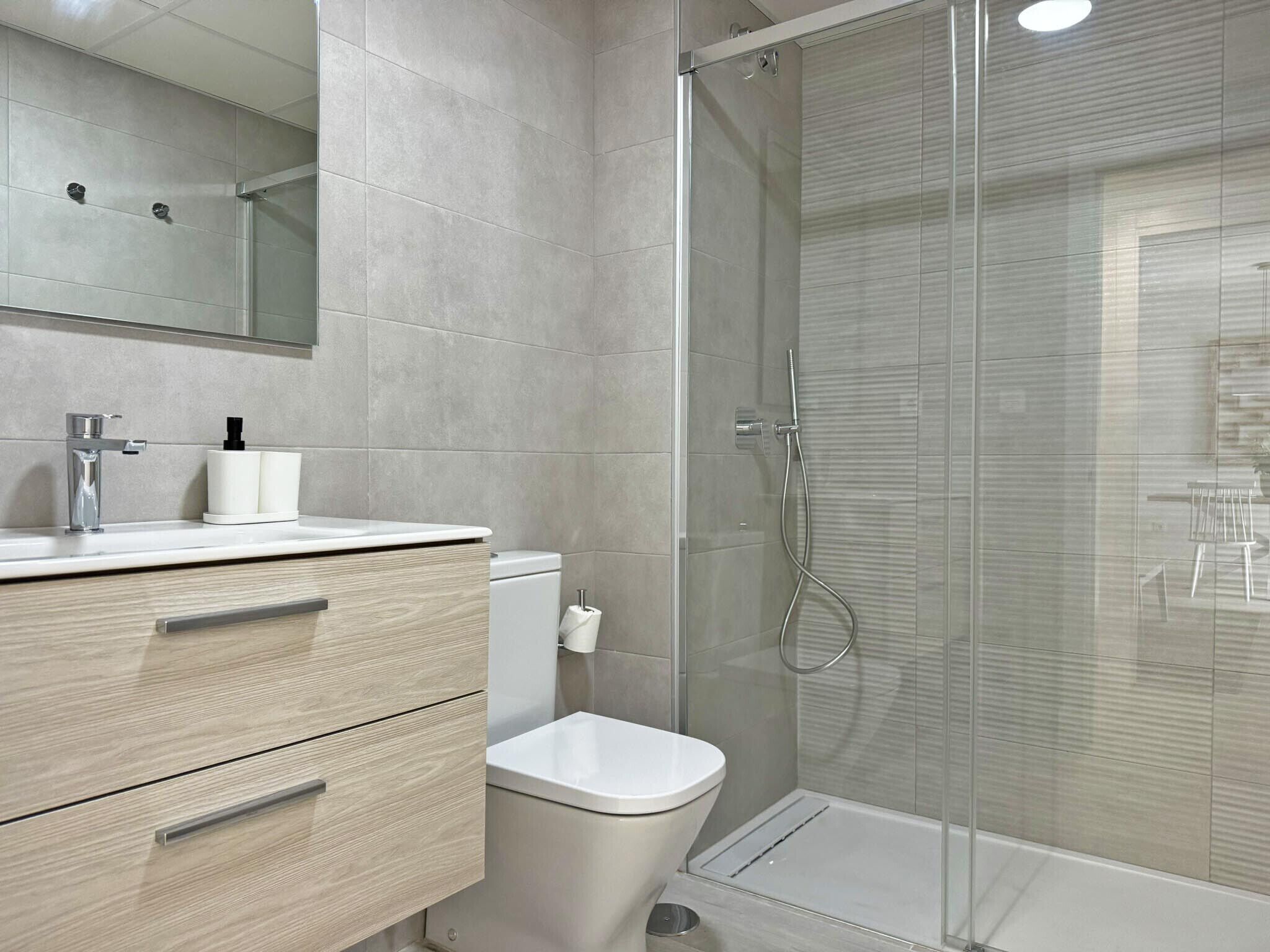 A modern bathroom with a glass shower enclosure, a white toilet, and a vanity with a mirror and a faucet.
