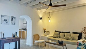 Un salon moderne avec un canapé, une table basse et un ventilateur de plafond. On aperçoit à l’arrière-plan un coin repas avec une table et des chaises.