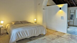 Une chambre à coucher avec un lit, deux lampes de chevet, un mur blanc et un plafond en bois.