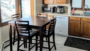 A compact kitchen with wooden cabinets, a dining table with chairs, a microwave, a coffee maker, and a window providing natural light. - Bright & Spacious Downtown 2 Bedroom Apt  w/ King bed! (Anchorage)