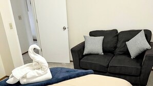 A hotel room with a bed, a black sofa with grey cushions, and a white door. - Bright & Spacious Downtown 2 Bedroom Apt  w/ King bed! (Anchorage)