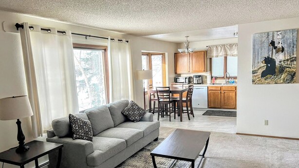 A living room with a grey sofa, a coffee table, and a dining area with wooden chairs and a kitchen in the background. - Bright & Spacious Downtown 2 Bedroom Apt  w/ King bed! (Anchorage)