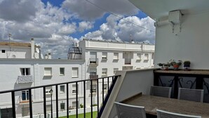 A balcony with a pool, white buildings in the background, and a clear sky.