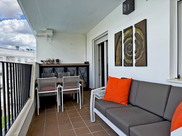 Un balcone con un divano bianco, due poltrone e un tavolo. Tre quadri astratti adornano la parete.