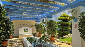 Un patio con una pérgola azul, plantas en macetas y una pared con un mural del sol y la luna.