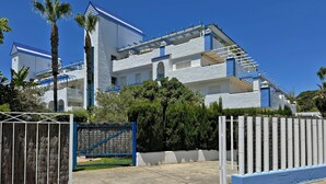 Un edificio moderno con fachada blanca y detalles azules, que presenta una entrada con reja y abundante vegetación.