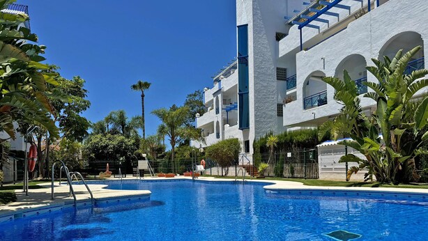 Una piscina rodeada por un edificio blanco con balcones y palmeras.