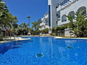 Ein Schwimmbad, umgeben von einem weißen Gebäude mit Balkonen und Palmen.