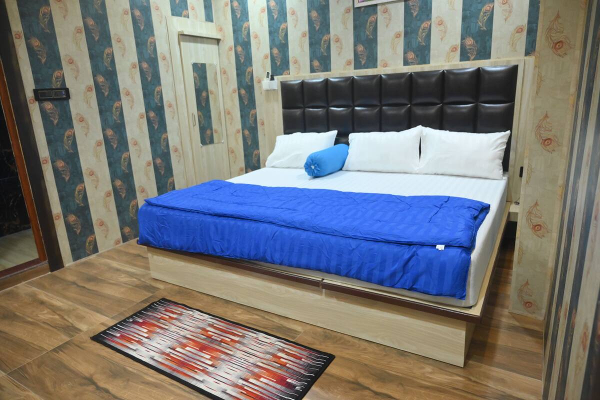 Ein Schlafzimmer mit einem Bett, blauer Bettwäsche, Holzboden und Wandpapier mit Muster.