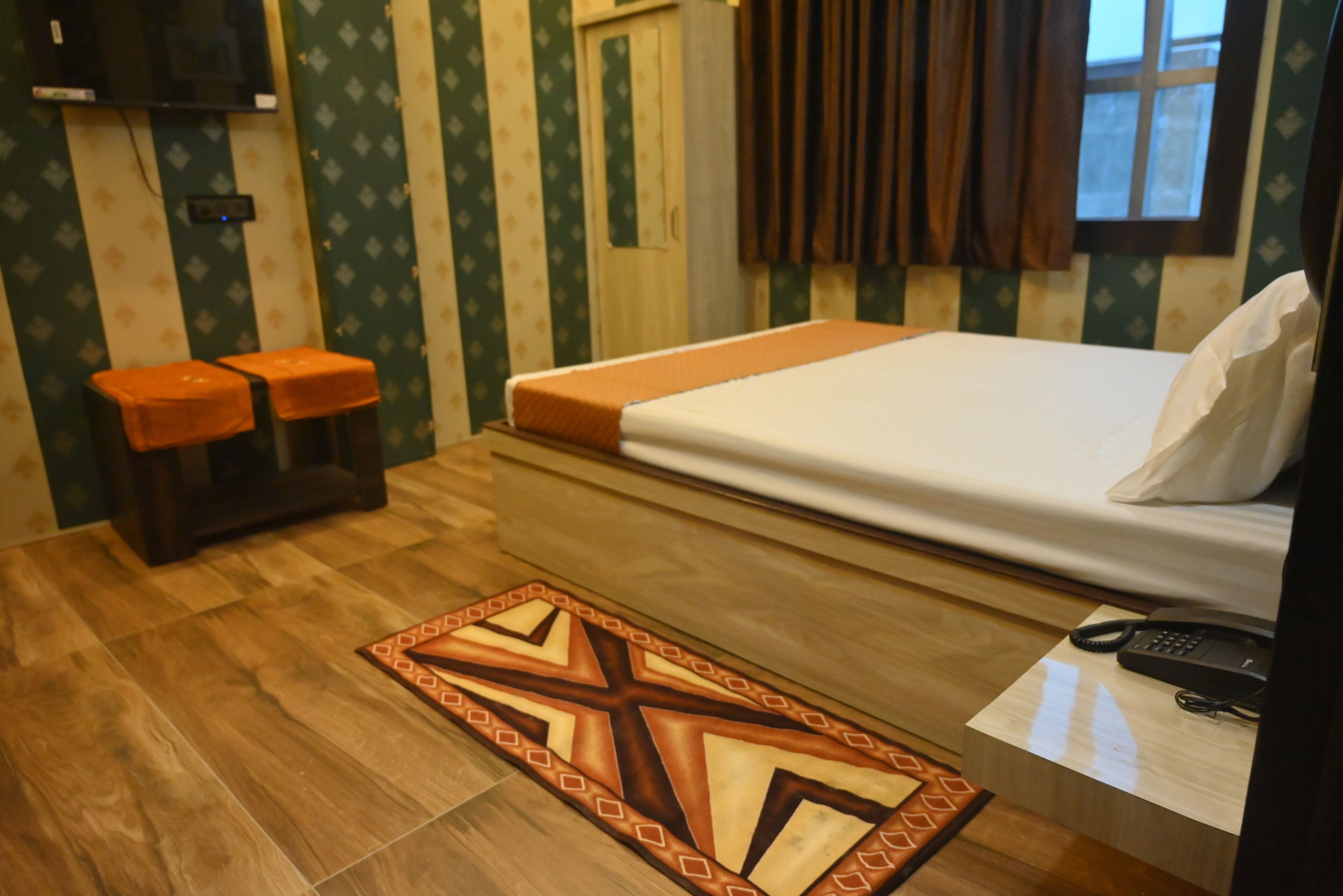 Una habitación de hotel con una cama, dos taburetes, un teléfono y una alfombra estampada.