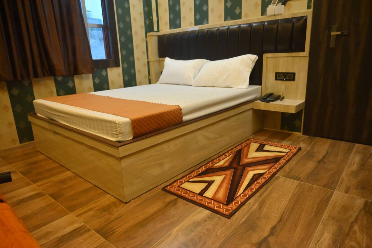 Ein ordentlich bezogenes Bett mit einer braunen Decke, ein Nachttisch mit einem Telefon und ein gemustertes Teppich auf Holzdielen.