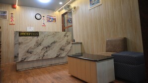 A reception area with a marble counter, wooden paneling, a clock, and a fan. - Hotel Prince (Gorakhpur)