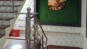 A staircase with a metal handrail, a red fire extinguisher, and a wall with a green artificial grass section. - Hotel Prince (Gorakhpur)