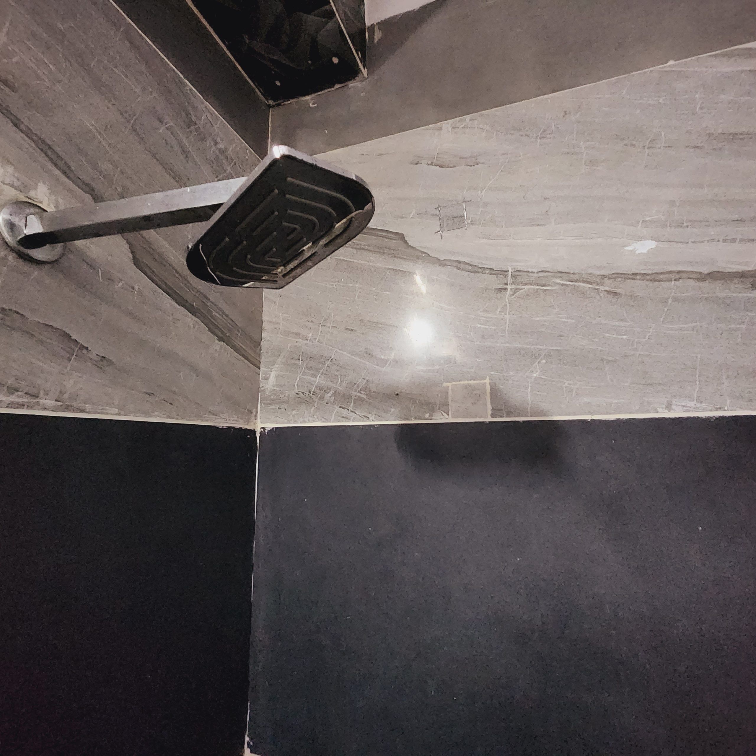 A corner of a room with a black and grey tiled floor, a metal fixture, and a wall with a textured surface.