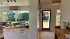 Een moderne keuken met een centraal eiland, witte kasten en uitzicht op de tuin door grote ramen.