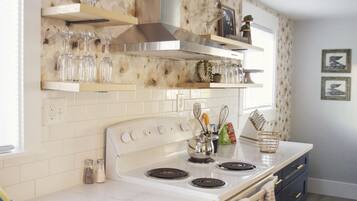 A kitchen with a white stove, a hanging pot rack, and a window with blinds.