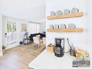 A modern living room with a sofa, coffee table, and decorative items. There is a coffee maker on the counter and a basket with snacks. - NEW OSU Reser Stadium Glamour- KING BEDS (Corvallis)