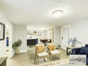 A spacious living room with a dining area, a kitchen in the background, and a large window with curtains.