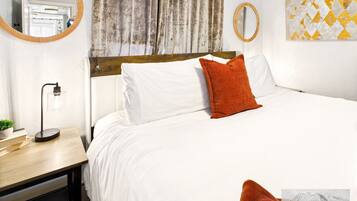 A hotel room with a bed, a nightstand with a lamp, a mirror, and a window with curtains.
