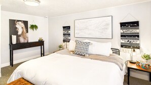 A bedroom with a large bed, a bedside table, a nightstand, a wall-mounted tapestry, and a framed artwork. - NEW OSU Reser Stadium Glamour- KING BEDS (Corvallis)