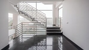 Um interior moderno com escada de vidro, paredes brancas e piso polido.