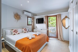 A modern bedroom with a large bed, a TV, an air conditioner, and a view of the outdoors.