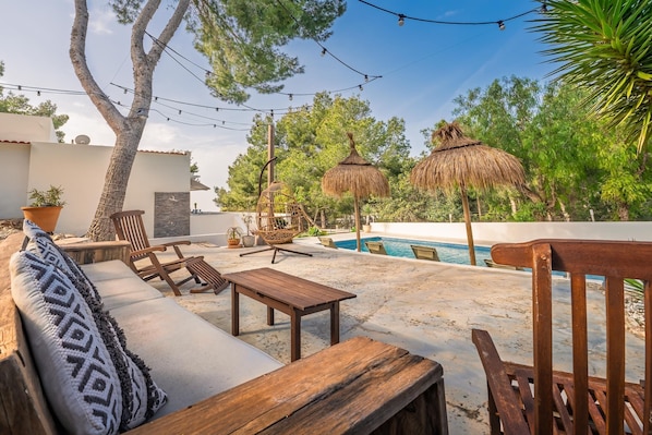 An outdoor seating area with a pool, wooden furniture, and thatched umbrellas.