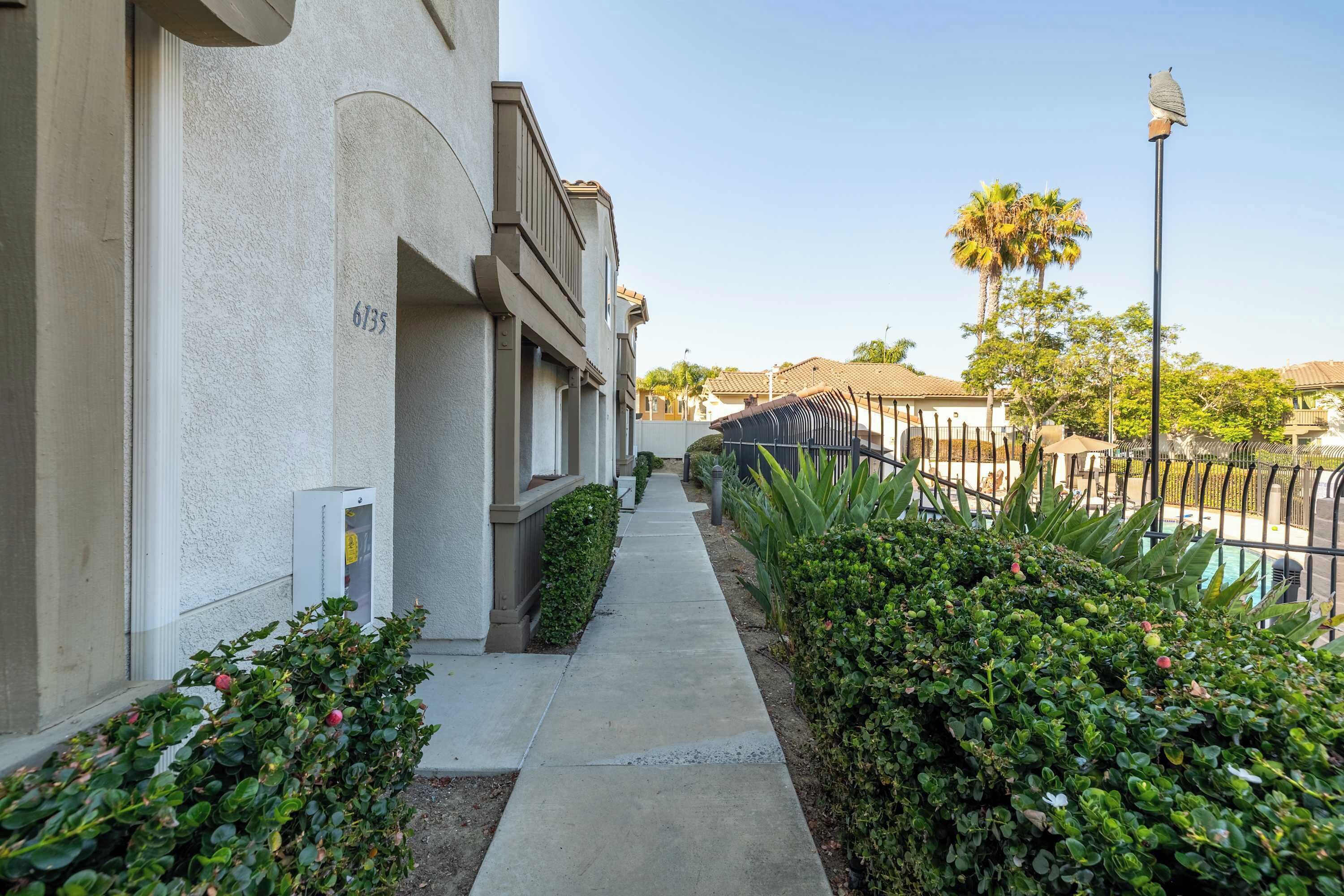 A residential building with a number 6735 on the side, a sidewalk, and a fenced pool area with palm trees.