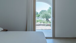 Ein Schlafzimmer mit Bett, einem Fenster mit Vorhängen und Blick auf eine Außenanlage mit Bäumen und einem Weg.