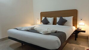 A neatly made bed with a wooden headboard, white bedding, and two bedside lamps. - SM Residency (Bhubaneshwar)