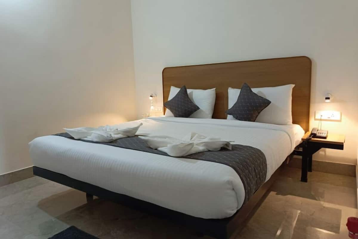 Uma cama bem arrumada com cabeceira de madeira, roupa de cama branca e duas luminárias laterais.