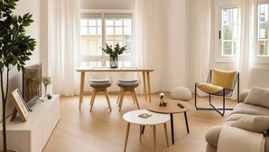 A modern living room with a wooden floor, a sofa, a coffee table, a dining table with chairs, and a plant. - 10 minutes from the beach! 10 minutes walk to the center.bright and quiet. (Pontevedra)