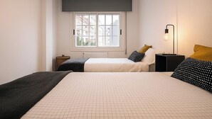 A bedroom with two beds, a window with a view of buildings, a radiator, a bedside table with a lamp, and a floor lamp. - 10 minutes from the beach! 10 minutes walk to the center.bright and quiet. (Pontevedra)