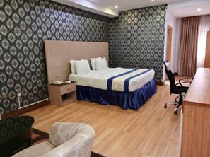 Una camera d'albergo con un letto, un comodino, una sedia e una scrivania con altra sedia.