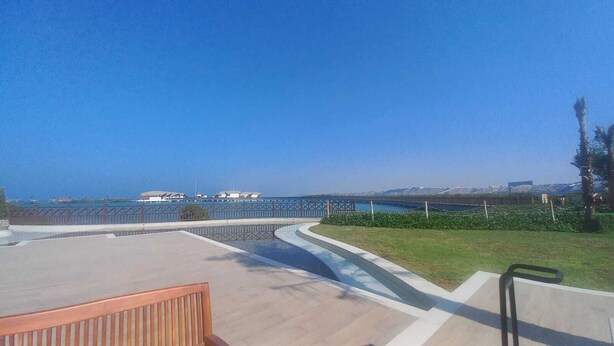 Une vue sur la côte, avec une promenade dallée, un banc en bois et une rambarde donnant sur la mer.