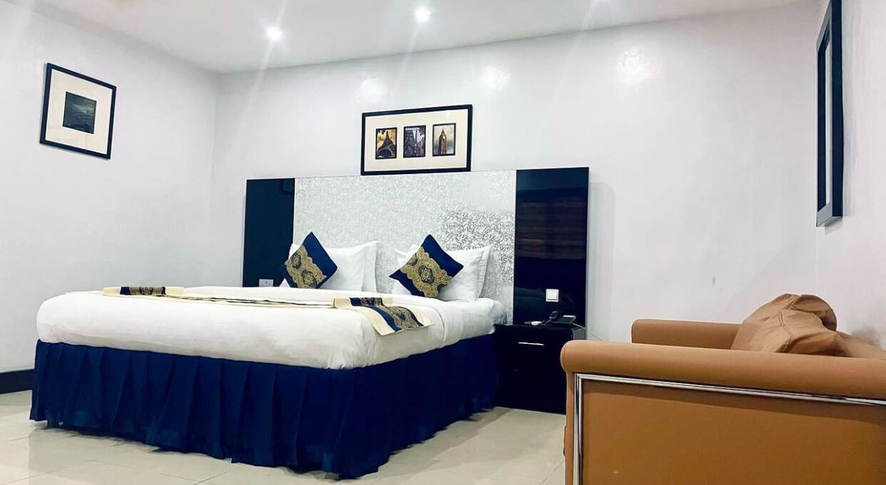A modern bedroom with a large bed, a nightstand, a brown armchair, and framed pictures on the wall.