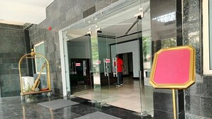 L’entrée d’un hôtel, avec une porte en verre, un comptoir d’accueil et un panneau indiquant « POUSSER ».